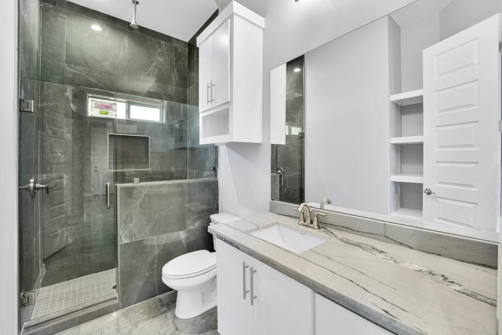 Bathroom with a glass shower enclosed in grey marble tile beside a white vanity with a marble counter