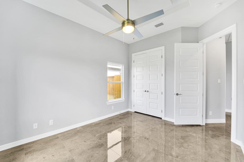 Empty primary bedroom with a vaulted ceiling, ceiling fan and double closet doors