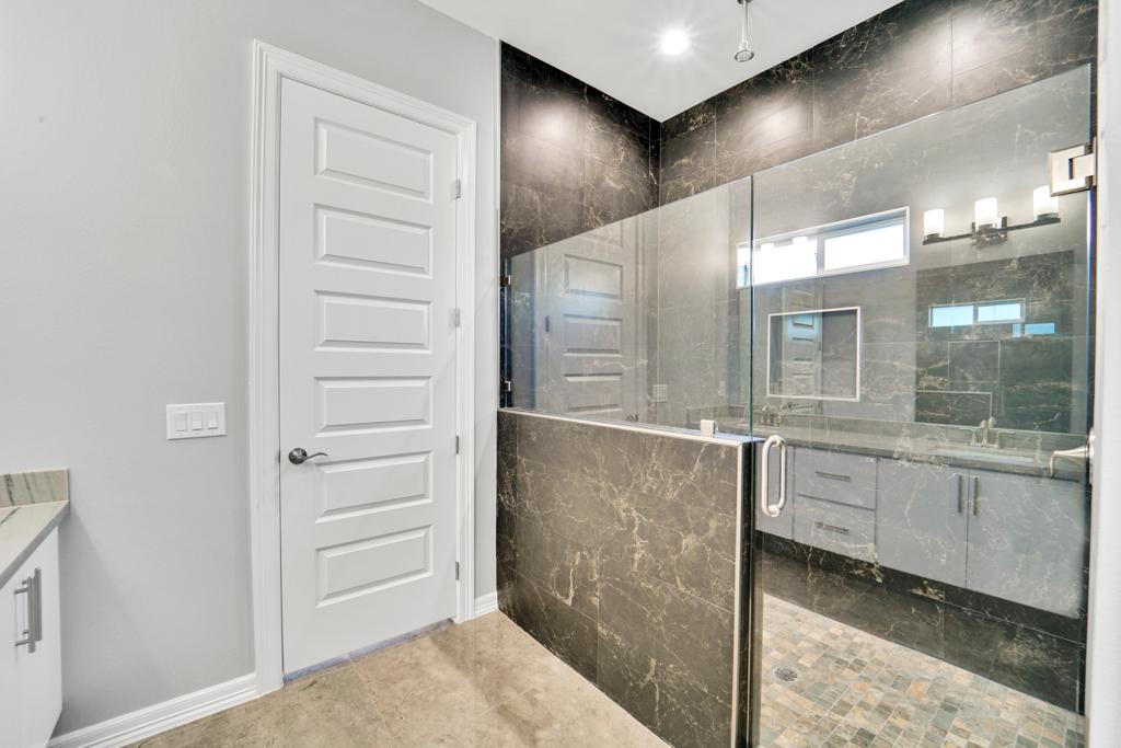 Primary bathroom with a black marble shower surround and a lit vanity mirror