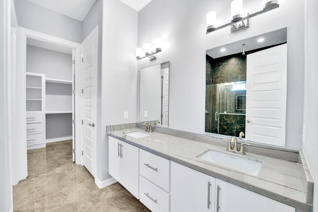 Double vanity with twin mirrors and sconces, beside an open walk-in closet with fitted shelving