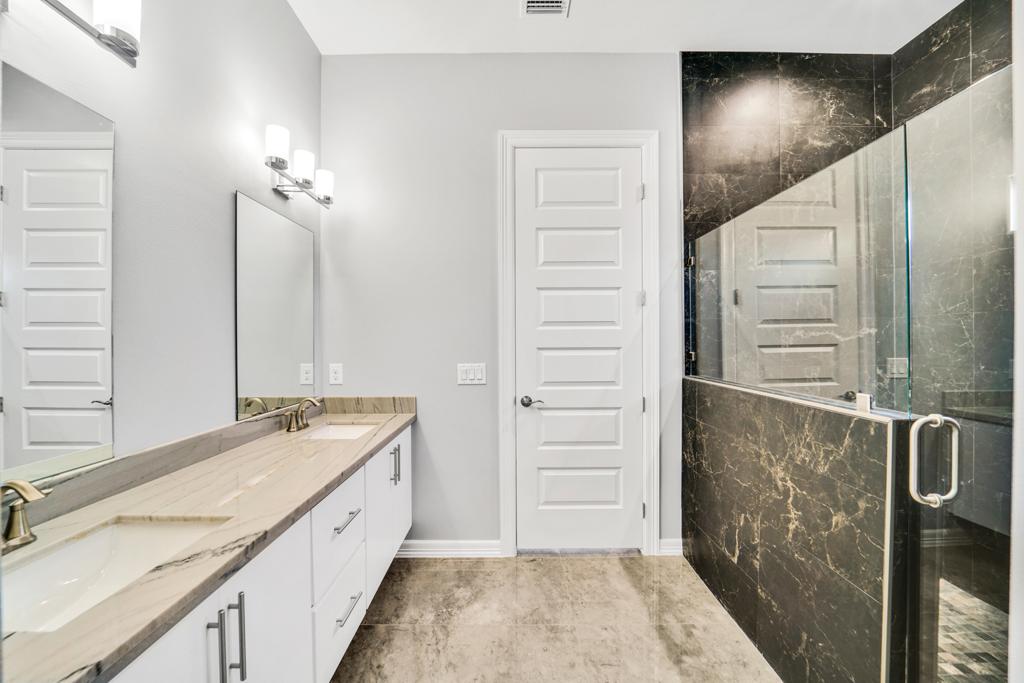Long double vanity with a marble counter facing a dark marble walk-in shower