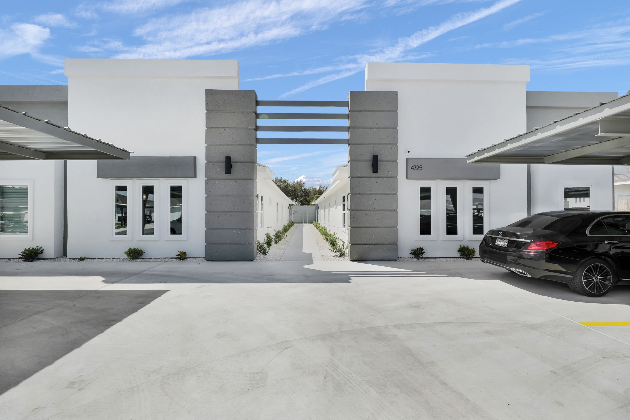 Gated entrance to a modern apartment court with white stucco pylons and a metal screen