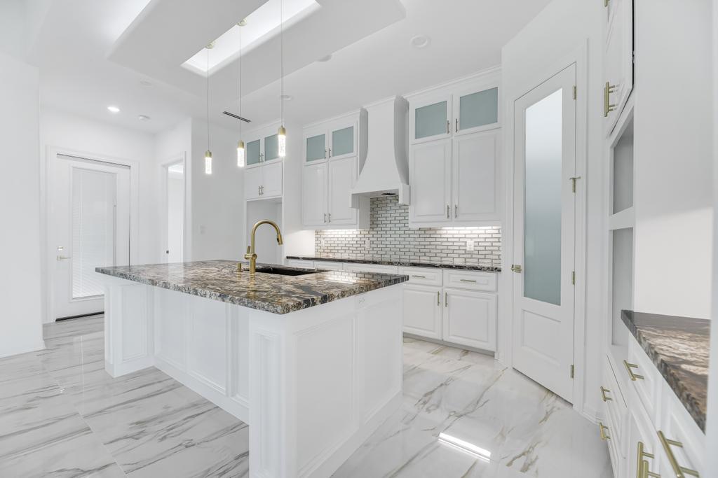Kitchen with a granite island, white shaker cabinets, brass fixtures and a glass-panelled pantry door